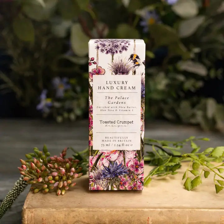 Luxury hand cream packaging with floral design on a wooden surface with greenery in the background