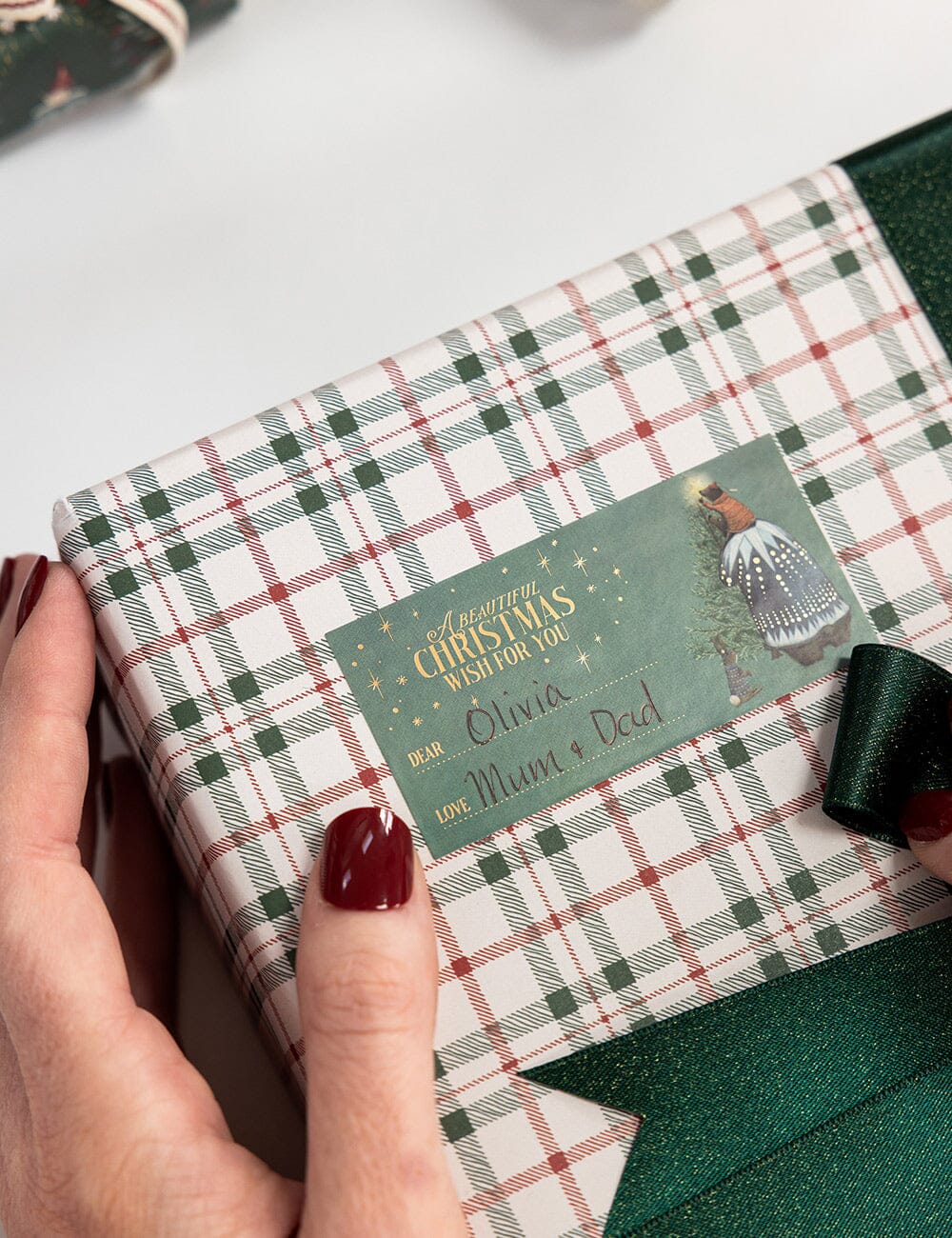 Gift box with plaid pattern and personalized Christmas card held by a hand.