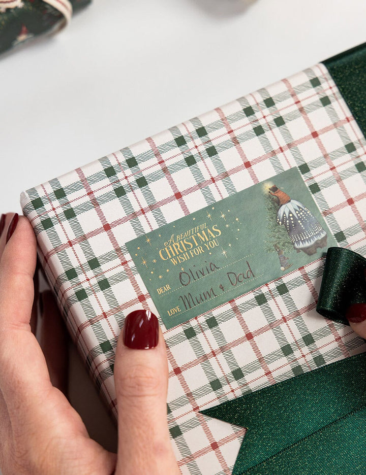 Gift box with plaid pattern and personalized Christmas card held by a hand.