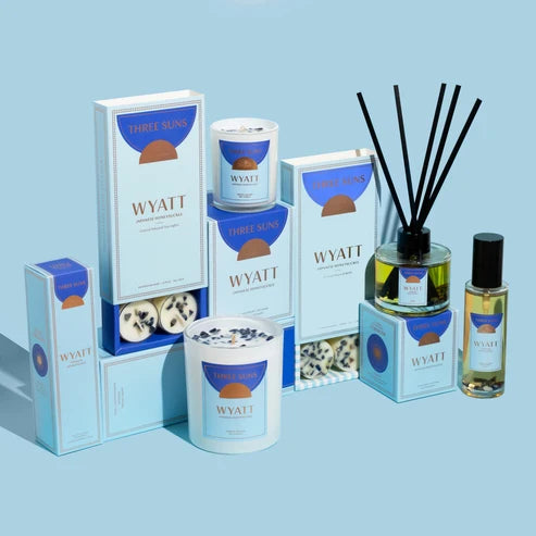 Three Suns Wyatt candles, diffusers, and packaging on a light blue background
