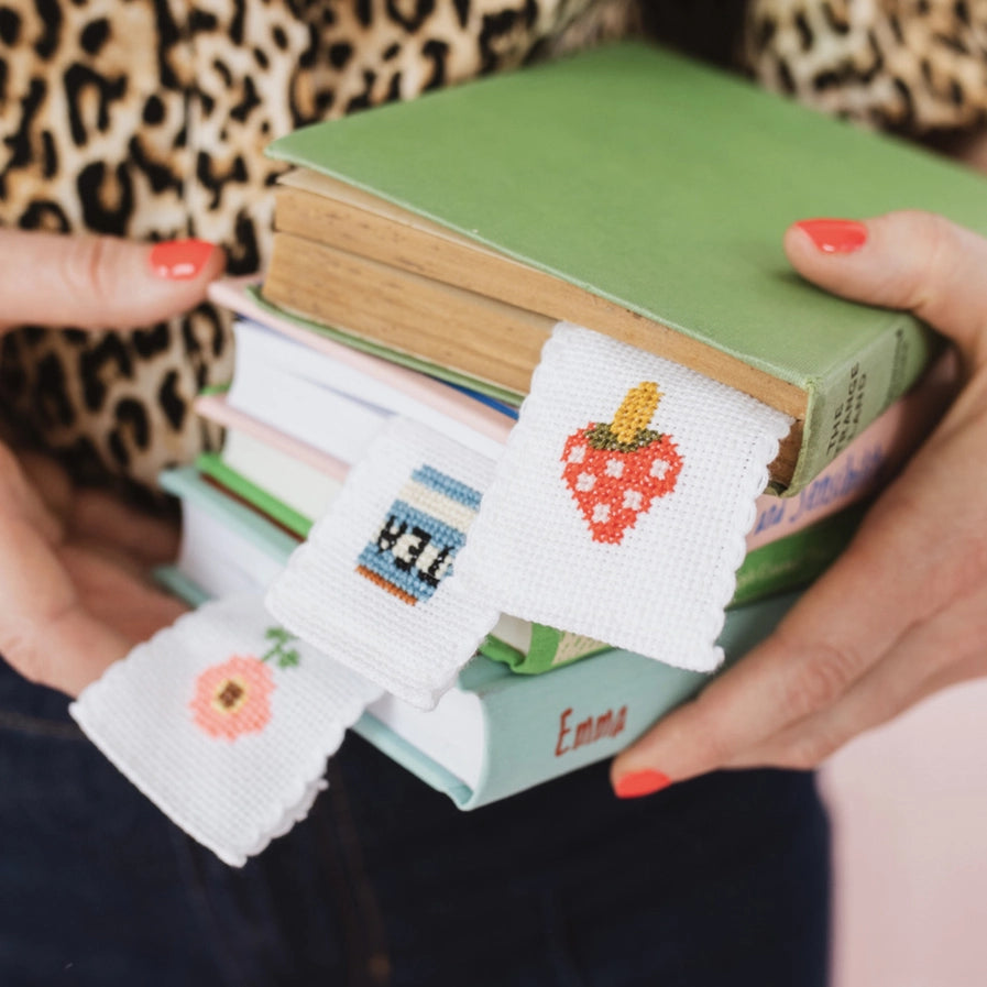 Stack of books held by a person wearing cross-stitched wrist warmers with various designs.