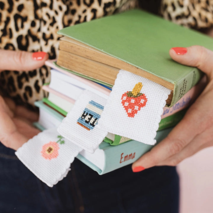 Stack of books held by a person wearing cross-stitched wrist warmers with various designs.