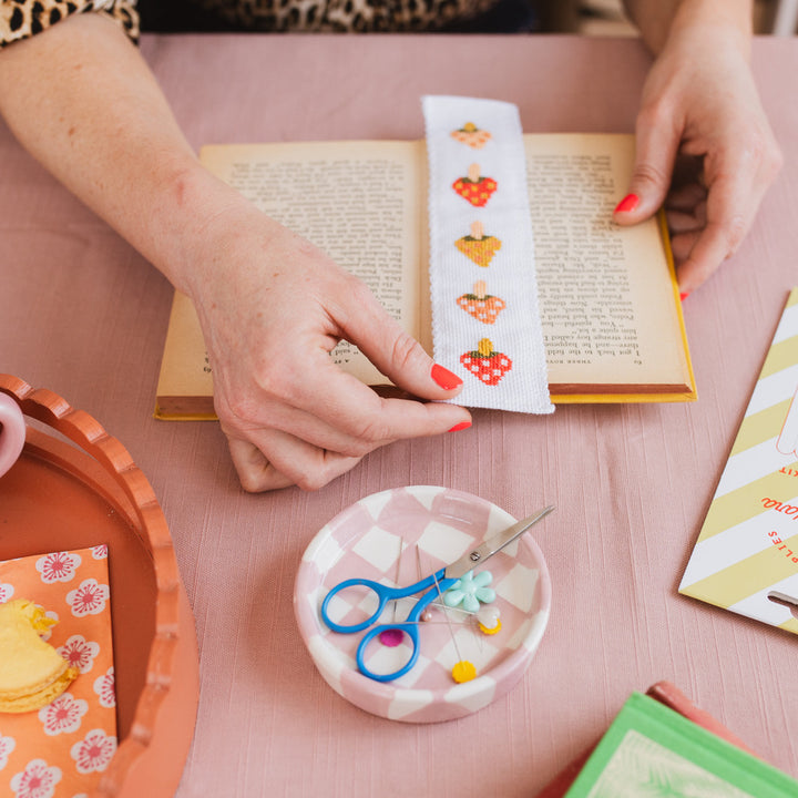 Person decorating a book with a colorful bookmark on a pink surface.