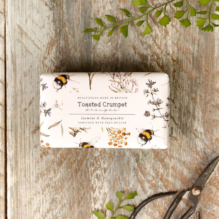 Bar of soap with a decorative label featuring bees and flowers on a wooden surface.