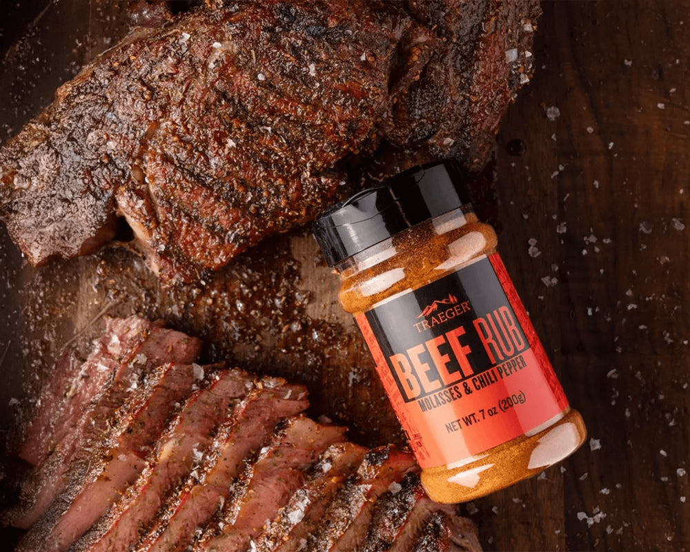 Bottle of beef rub on a wooden surface with seasoned meat.