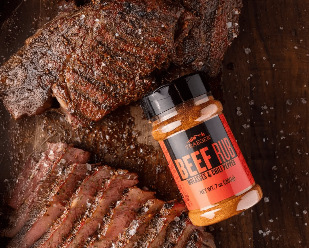 Bottle of beef rub on a wooden surface with seasoned meat.