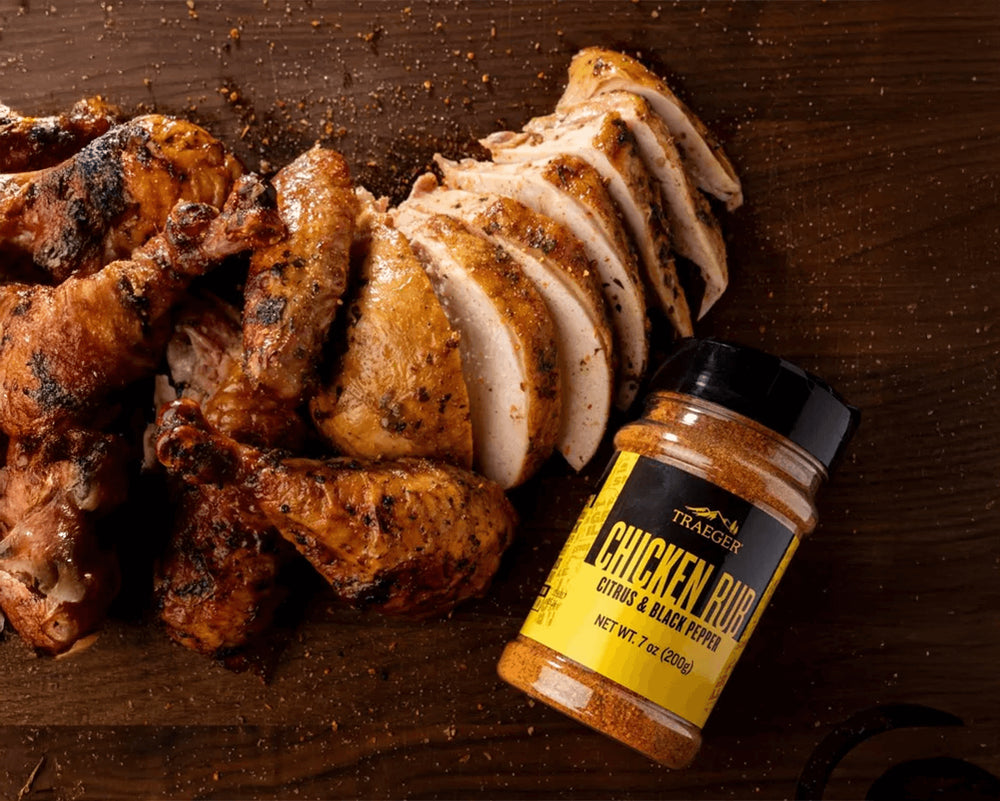 Sliced chicken breast and wings with a jar of Traeger's Chicken Rub on a wooden surface