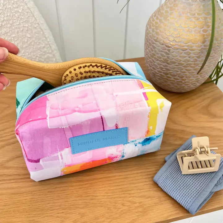 Colorful makeup bag with a brush and towel on a wooden surface, featuring &