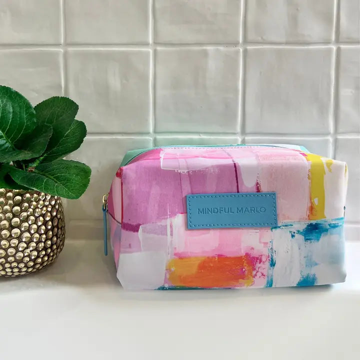 A rectangular zip pouch with a colorful abstract watercolor print in pink, blue, orange, yellow, and white, featuring a light blue leather patch with the brand name &