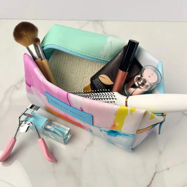 Colorful makeup bag with various items including brushes and a razor on a marble surface.