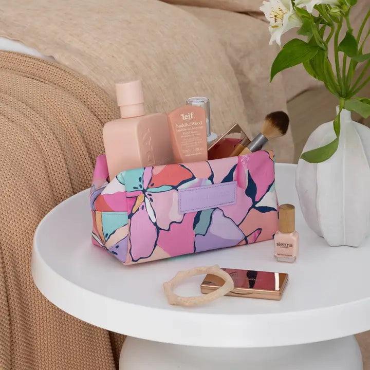 Floral-patterned makeup bag on a table with various cosmetic items and a vase with flowers.