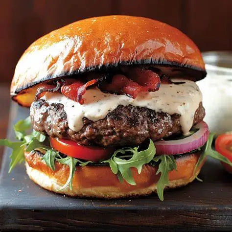 Delicious hamburger with bacon, lettuce, tomato, and cheese on a wooden cutting board.
