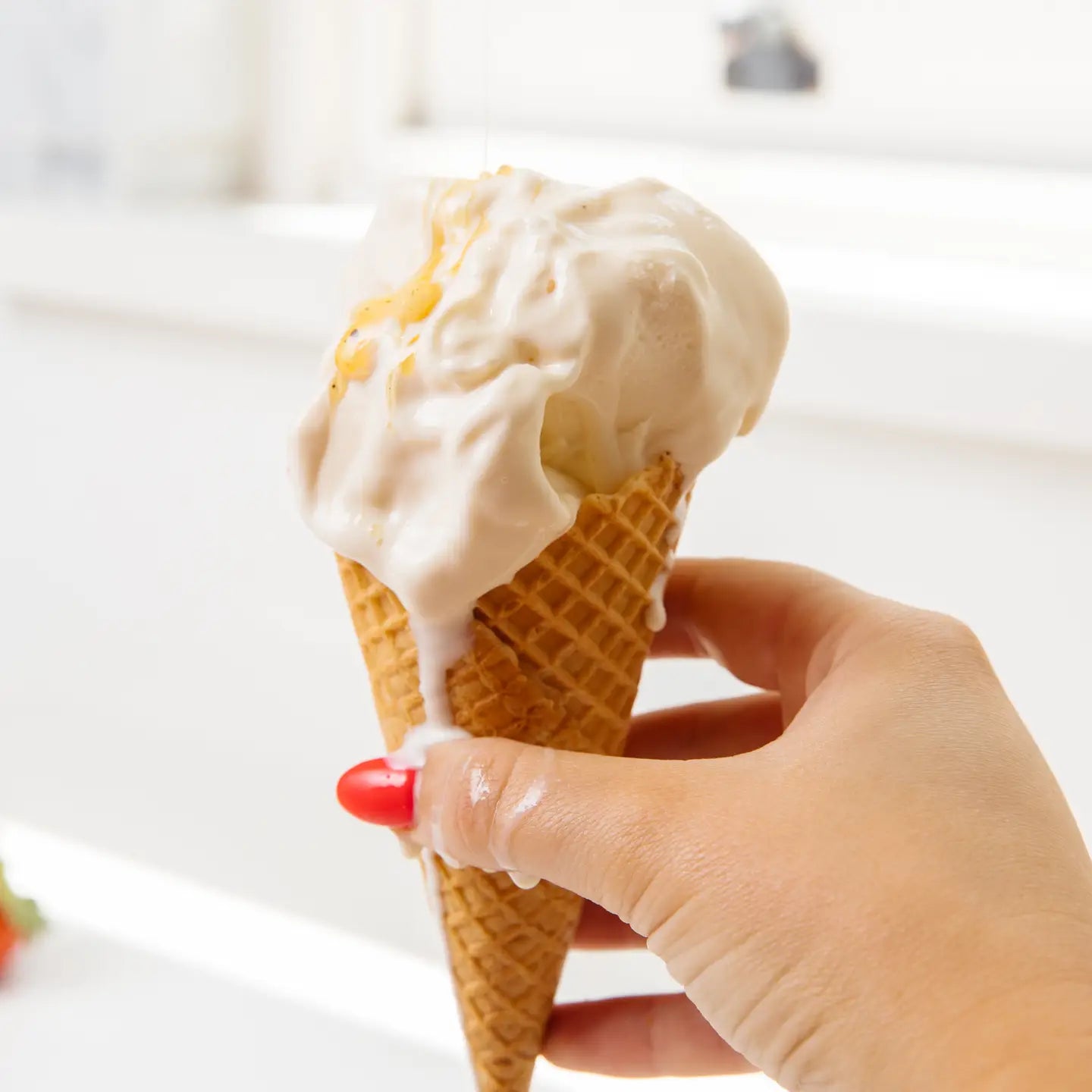 Hand holding a waffle cone with ice cream against a blurred background