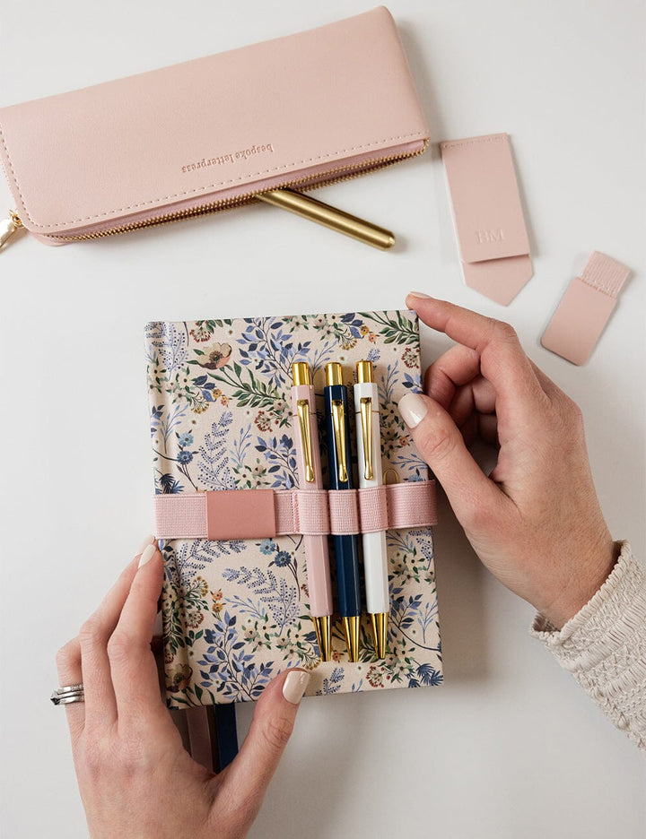 Floral notebook with pens held by a hand on a white background