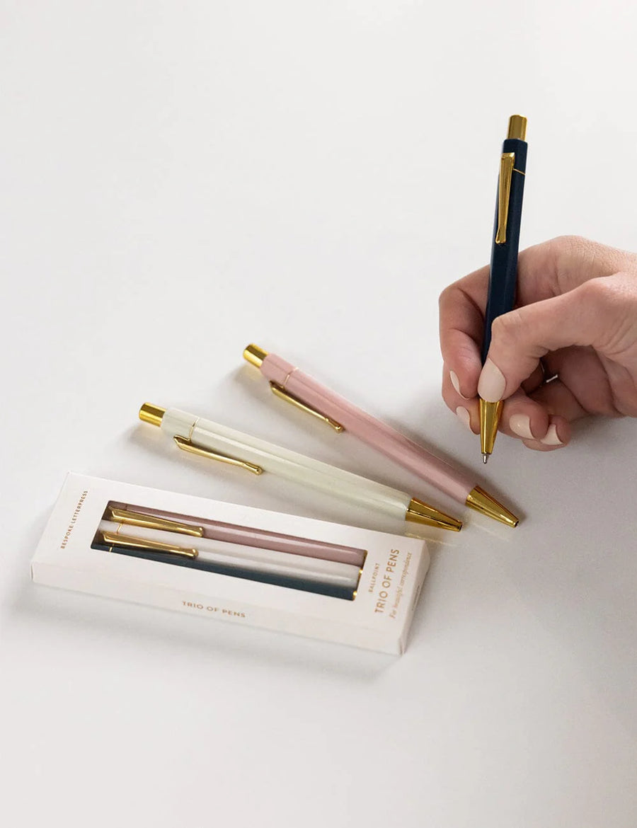 Hand holding a pen with other pens and packaging on a light background