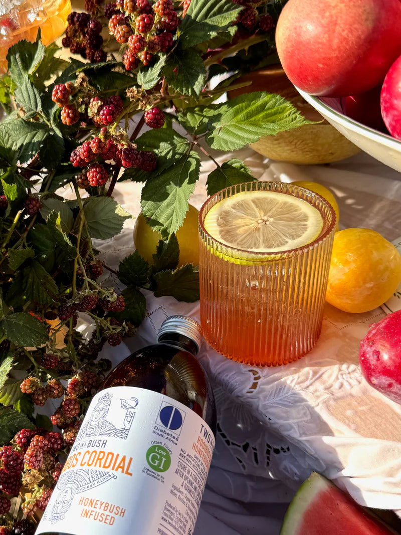 Cocktail with lemon slice, bottle of Cordial, and fruits on a table.