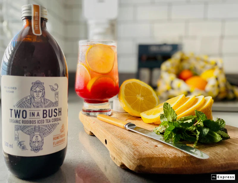 Two in a Bush bottle with a glass of iced tea and lemon slices on a kitchen counter.