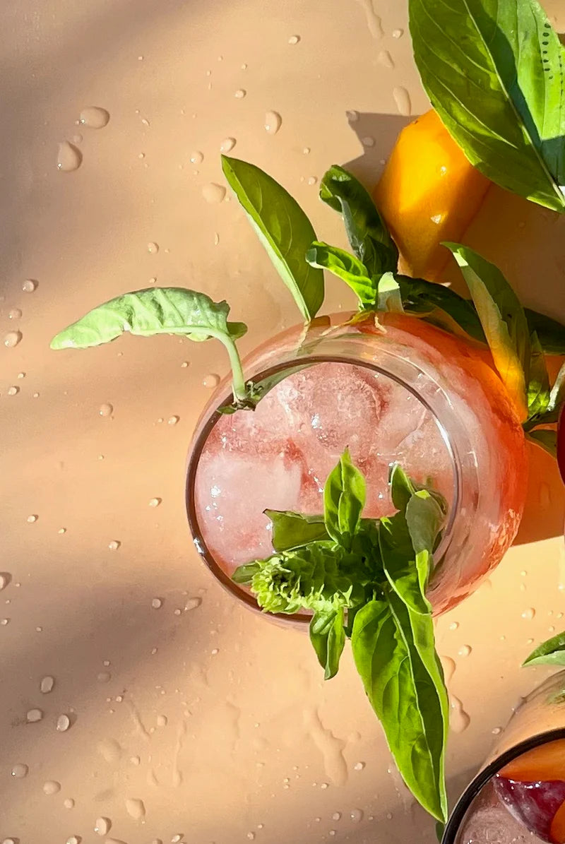 Iced tea with basil leaves and peaches on a wet surface