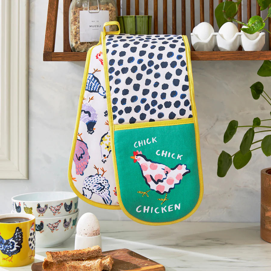 Oven mitt with chicken design hanging on a wall in a kitchen setting.