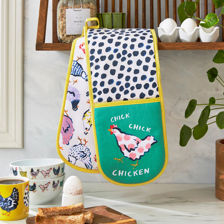 Oven mitt with chicken design hanging on a wall in a kitchen setting.