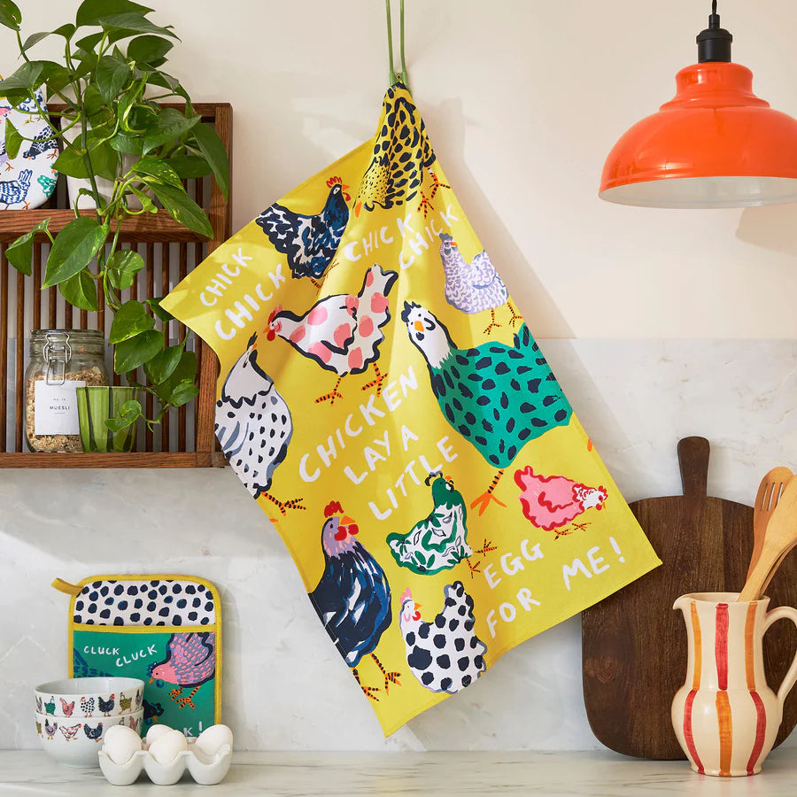 Colorful kitchen towel with chicken design hanging on a hook in a kitchen setting.