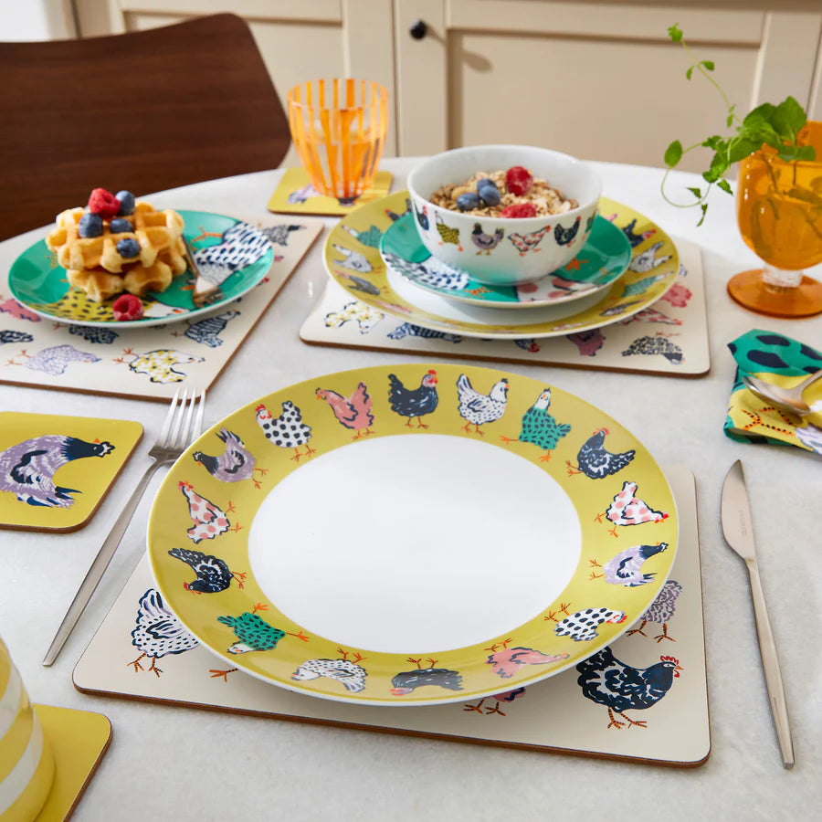 Dining table setting with colorful plates, cups, and waffles on a white tablecloth.