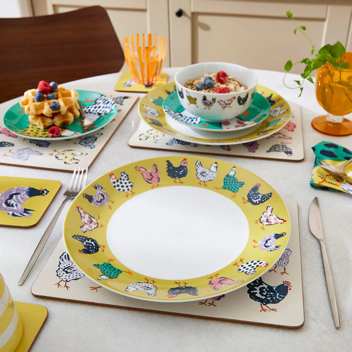 Dining table setting with colorful plates, cups, and waffles on a white tablecloth.