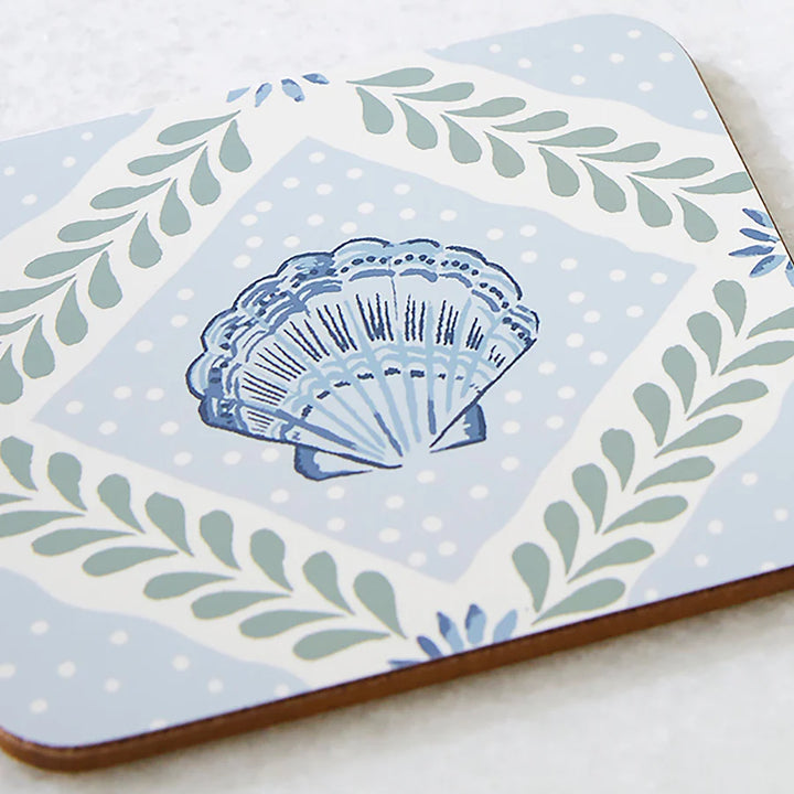 Decorative tile with a blue shell design on a light blue background with green leaves.