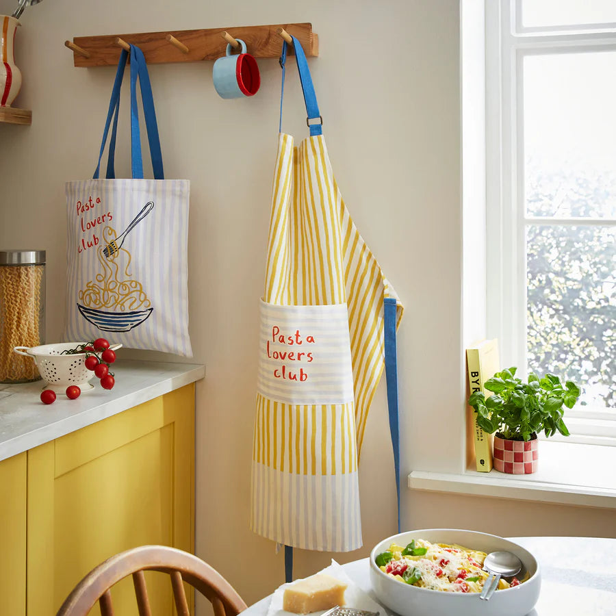 Kitchen scene with 'Pasta Lovers Club' apron and tote bag hanging on a rack.