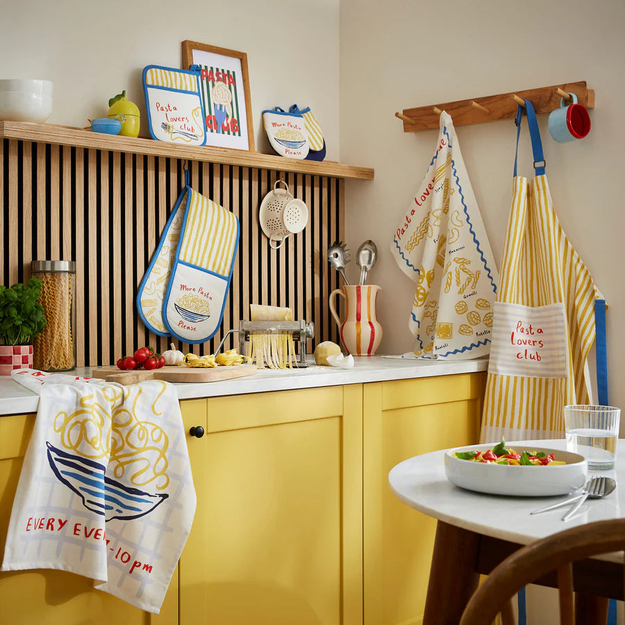 Kitchen with yellow cabinets, various kitchen towels, and utensils.
