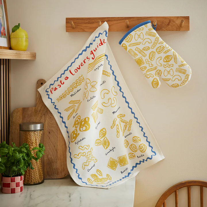 Cotton tea towel with pasta shapes on it hanging on a hook in a kitchen
