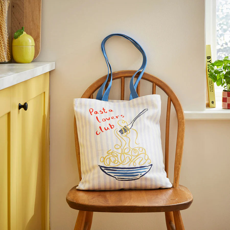 Tote bag with 'Pasta lovers club' design on a wooden chair against a light-colored wall.