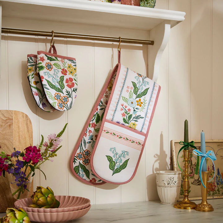 Floral-patterned oven mitts hanging on a rack in a kitchen setting.