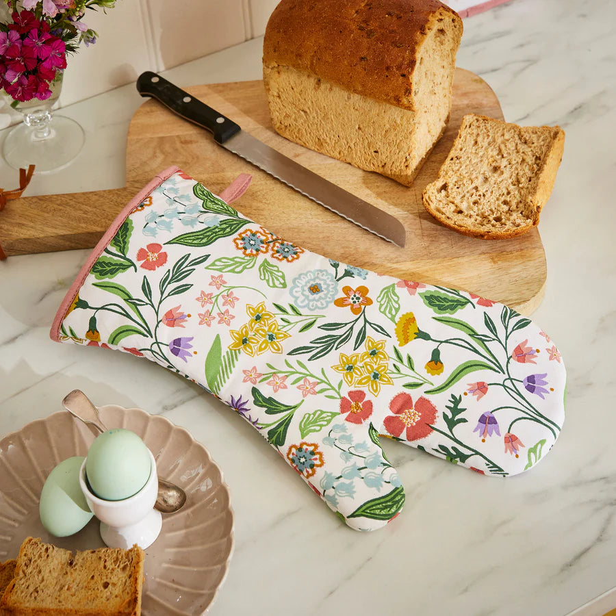 Floral oven mitt on a marble surface with bread and eggs.