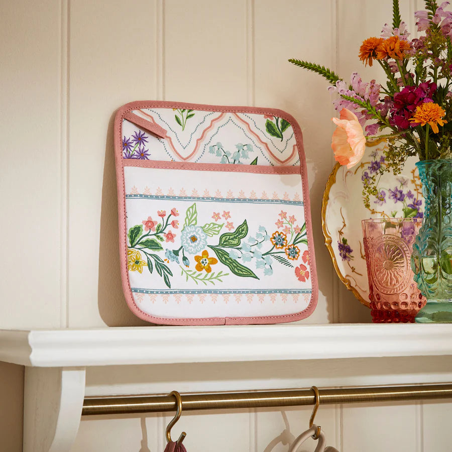 Floral-patterned pot holder on a white surface with a vase of flowers in the background.