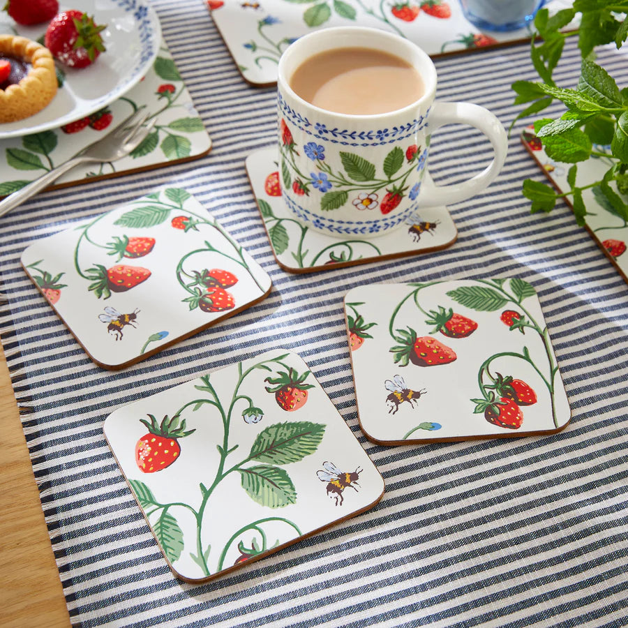 Set of strawberry-themed coasters with a cup of tea on a striped tablecloth.