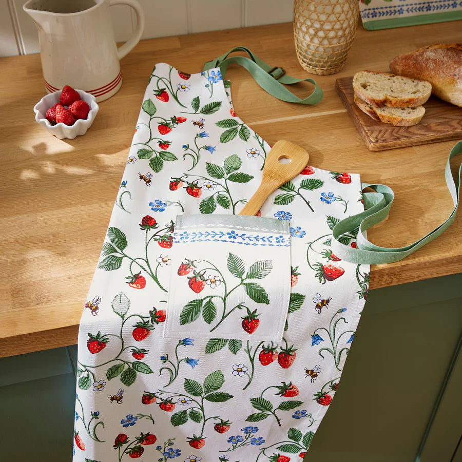 Kitchen apron with strawberry pattern on a wooden table with bread and fruit.