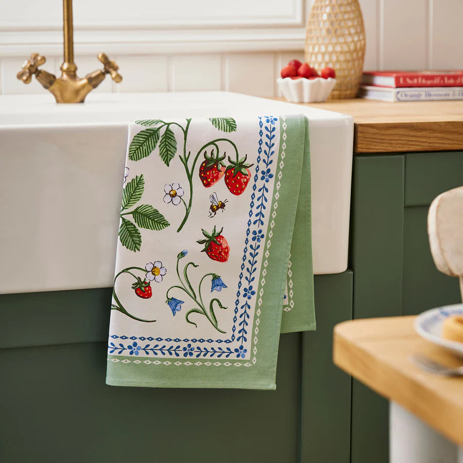 Decorative kitchen towel with strawberry design hanging over a green cabinet.
