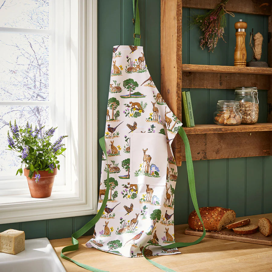 Apron with nature-themed design hanging on a wooden shelf in a kitchen.