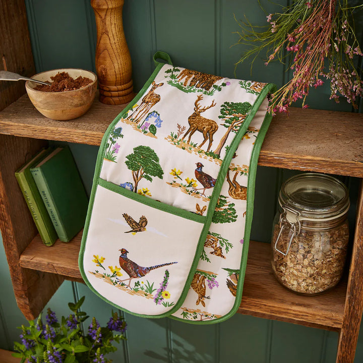 Decorative oven mitt with nature-themed design on a wooden shelf.