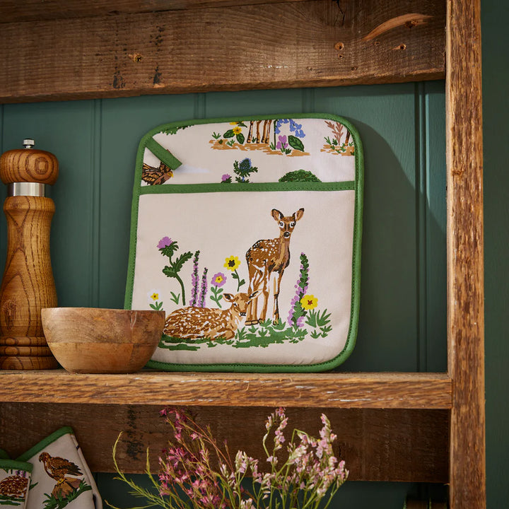 Decorative pot holder with deer design on a wooden shelf against a green wall.