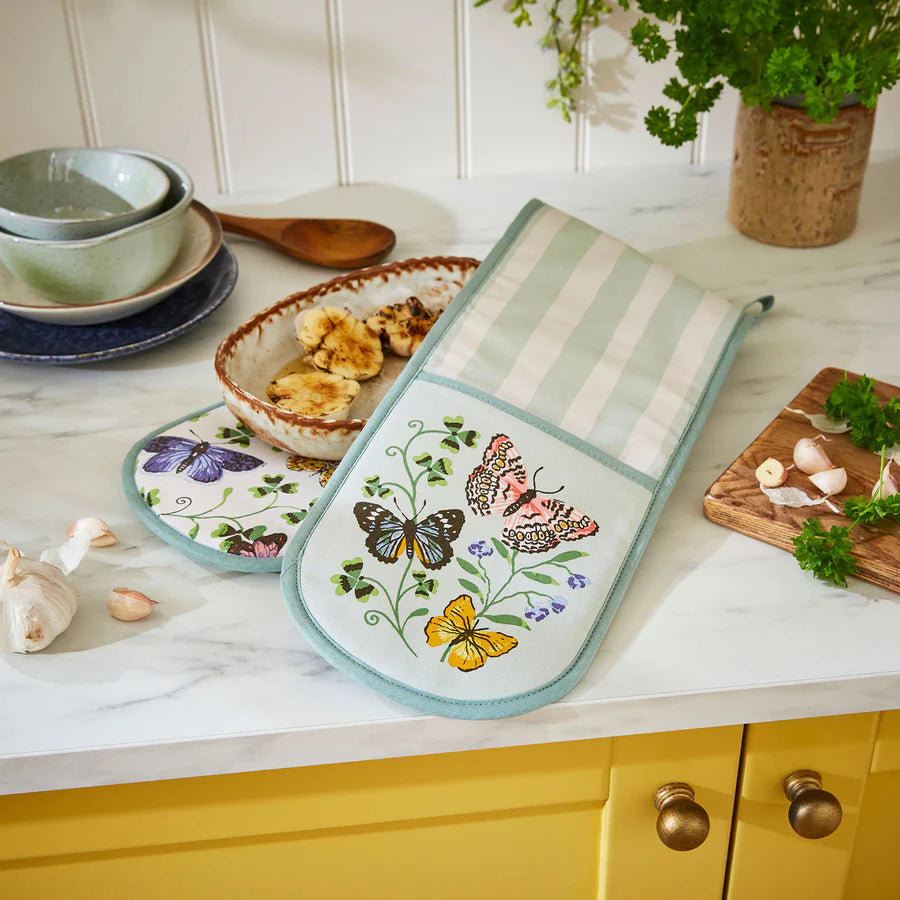 Butterfly-themed oven mitt and pot holder on a kitchen counter with food and decor.