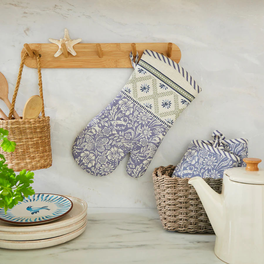 Decorative oven mitts with floral patterns hanging on a wooden rack in a kitchen setting.