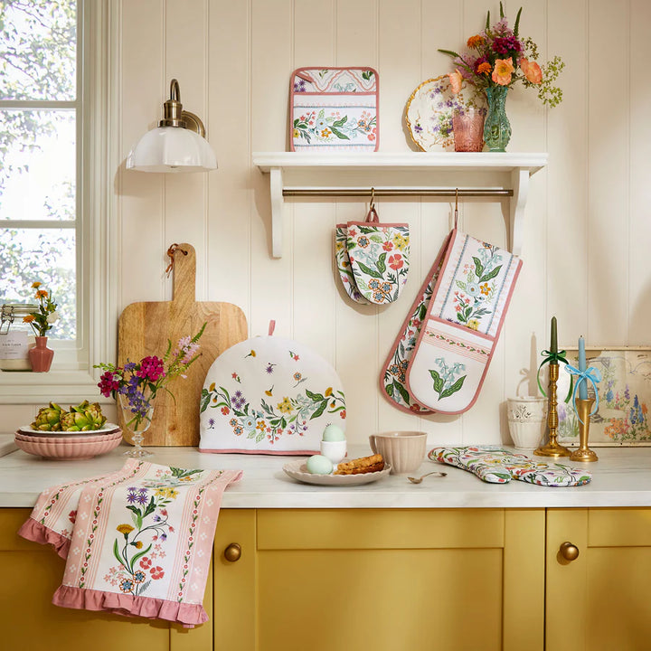 Kitchen scene with floral kitchen towels, oven mitts, and trivets on a yellow cabinet.
