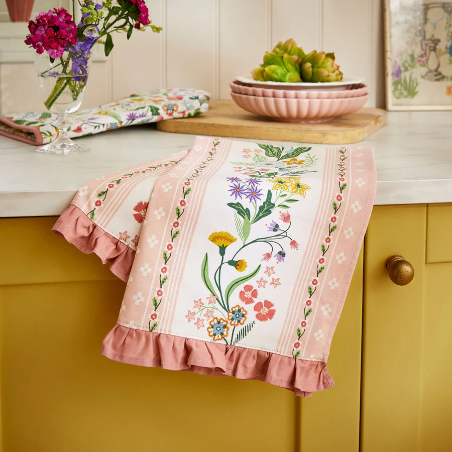 Floral tea towel hanging on a yellow cabinet with a kitchen setting in the background.