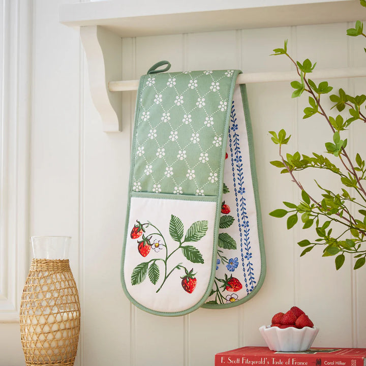Pair of oven mitts with floral and strawberry designs hanging on a white wall.