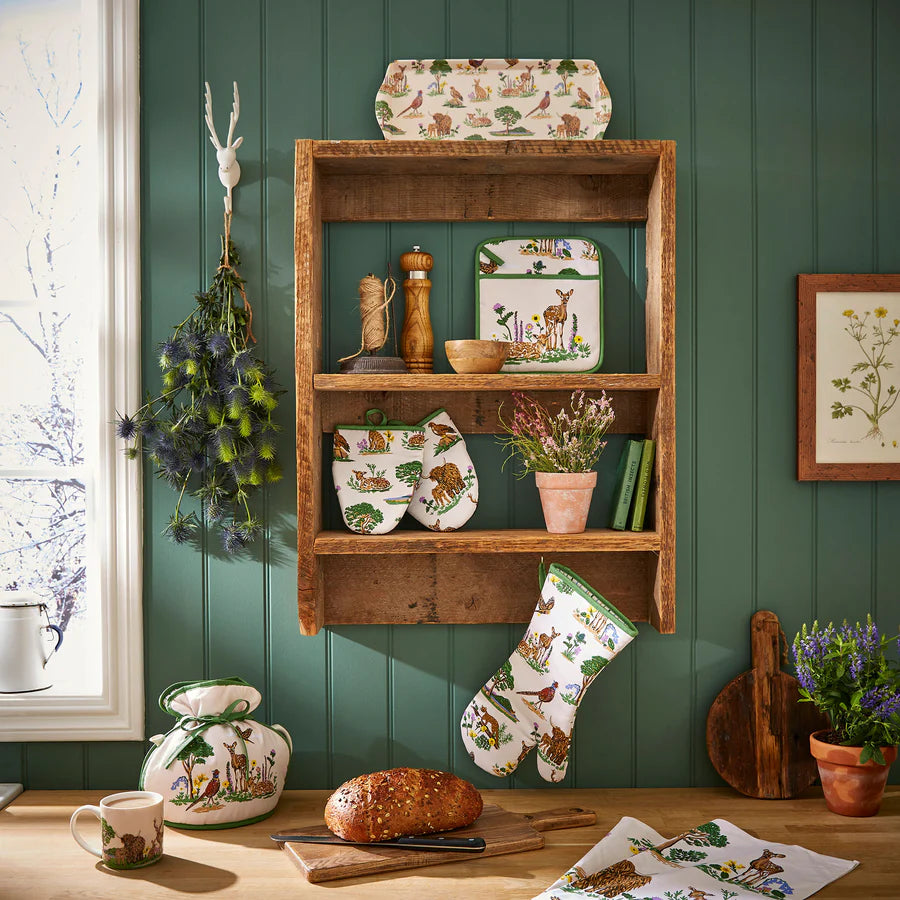 Wooden shelf with decorative items against a green wall, including a mug, bread, and a plant.