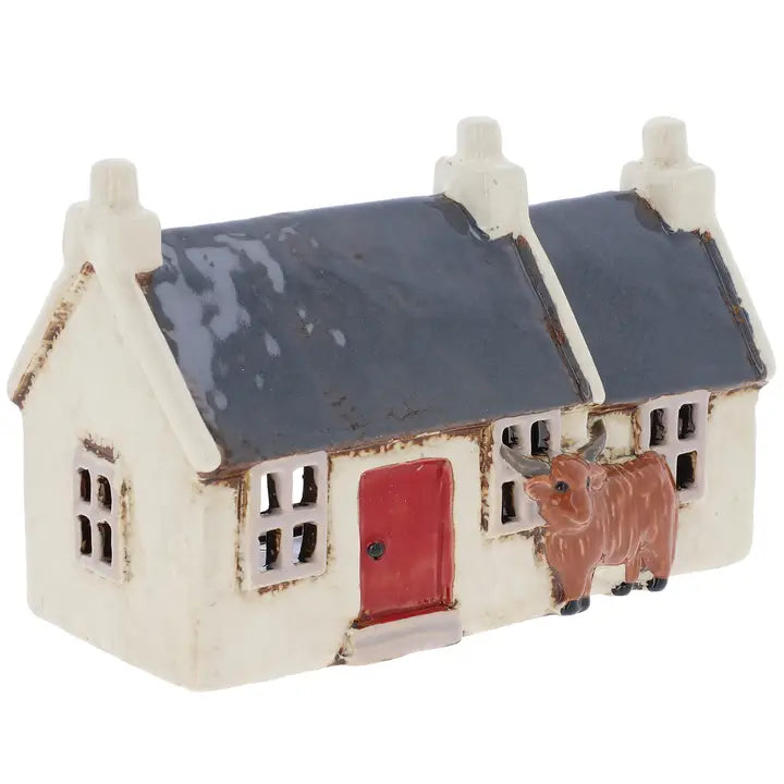 Small ceramic house  tealight holder  with a red door and cow figure on a white background