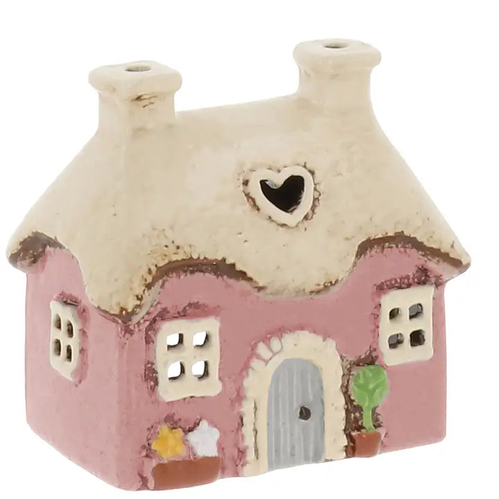 Small ceramic house with pink body, white roof, and decorative elements on a white background