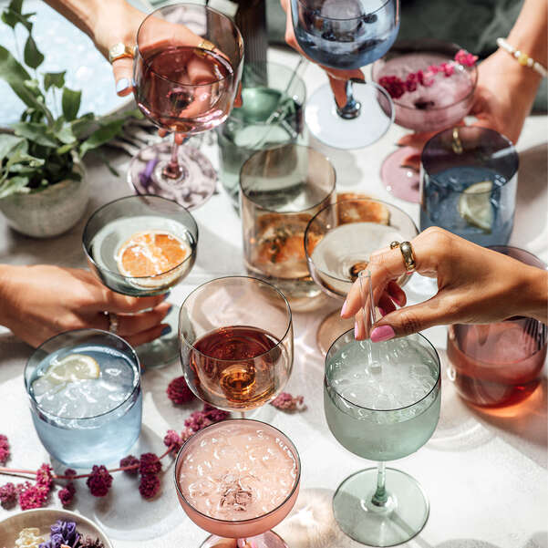 People holding glasses of colorful drinks at a table with flowers and plants.